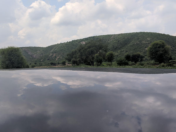 The reflective lake is the roof of a very clean car. It is polished so well that it creates the illusion of a very calm lake reflecting the sky and the clouds.