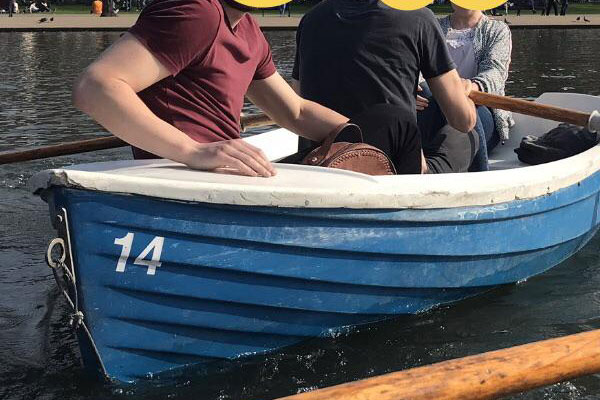 The man on the left is not standing in the water next to the boat. He is sitting with his friends in the boat.